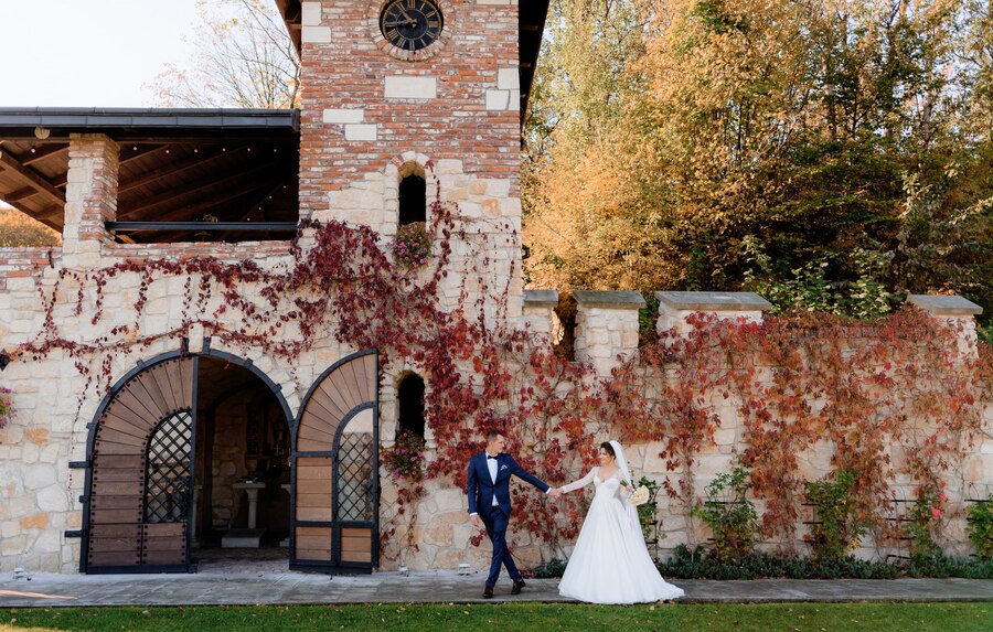 happy-groom-bride-are-holding-hands-together-walking-front-old-stone-building-warm-autumn-day_8353-11100